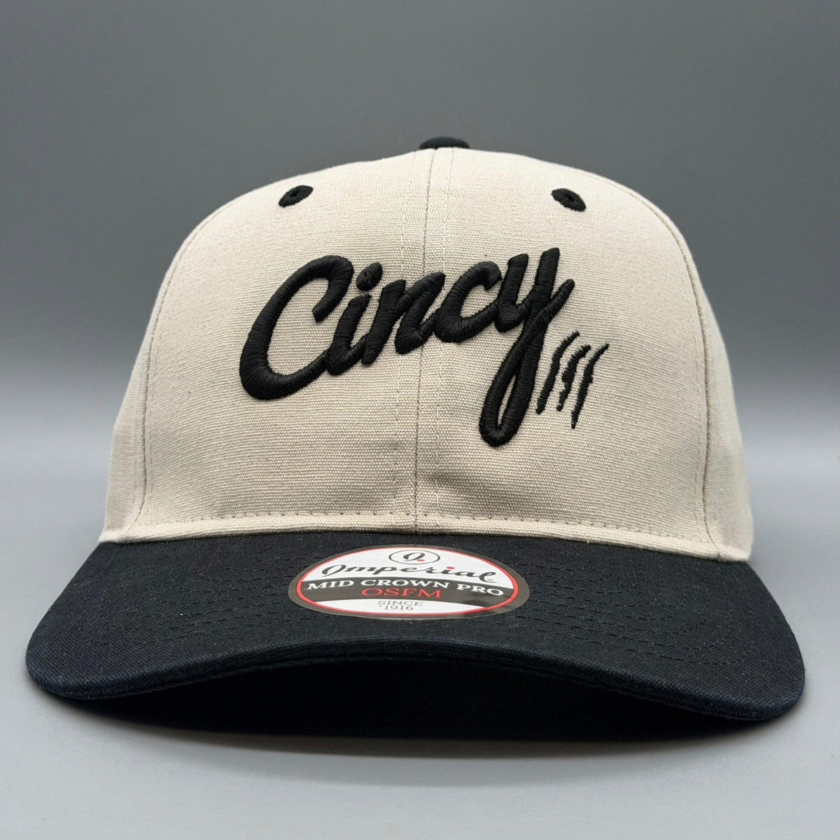 Angled view of the putty and black Washed Cotton Two Tone hat with puffed black Cincy script logo