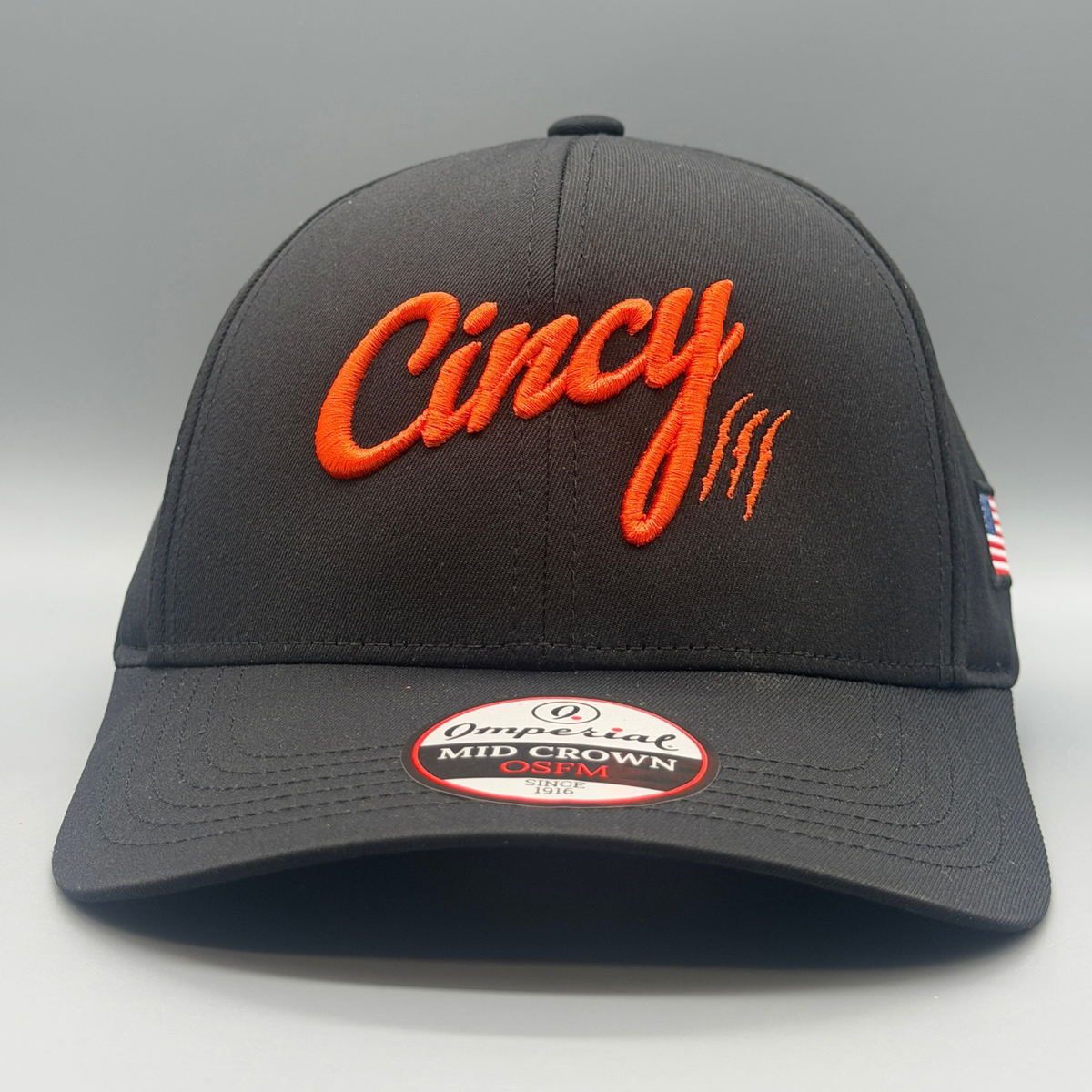 Angled view of The Casual Mid-Crown black cap with puffed orange Cincy script logo and American flag side patch