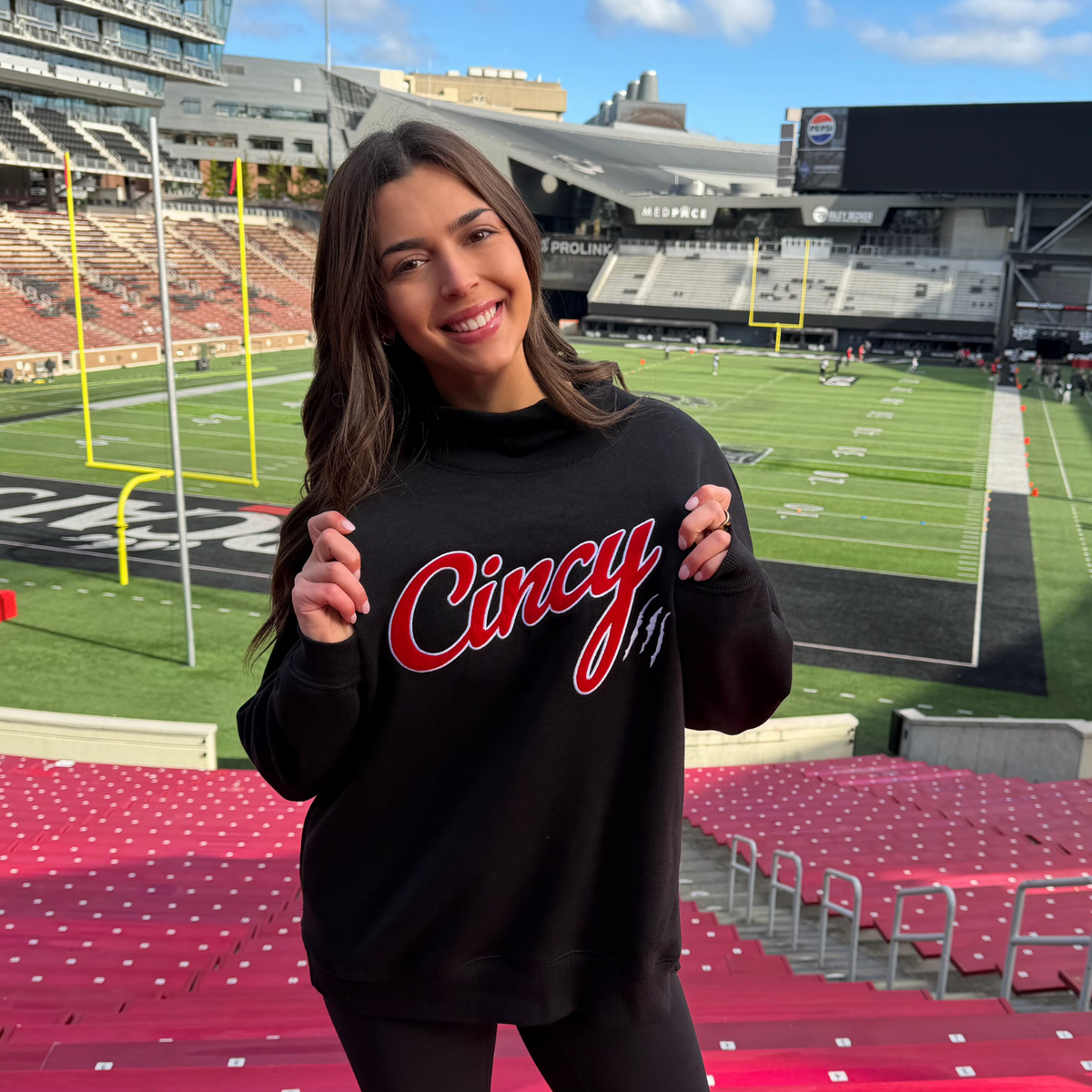 Black mock neck sweatshirt with red Cincy script, white outline and white claw marks, front view on model