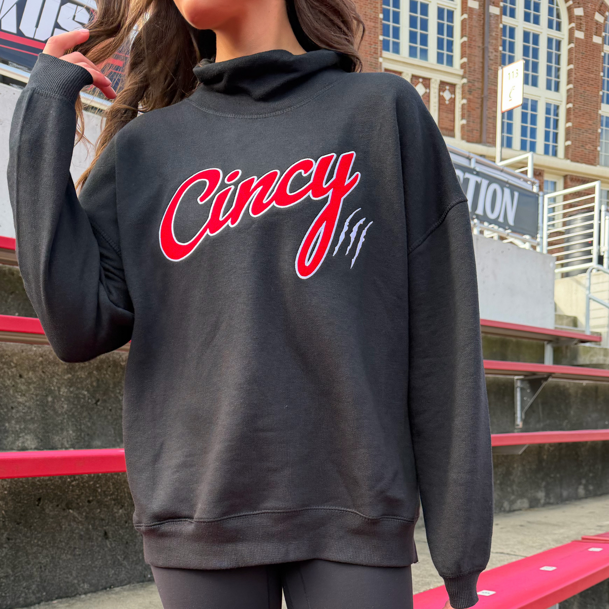 Close-up of red Cincy script, white outline and claw marks on black mock neck sweatshirt